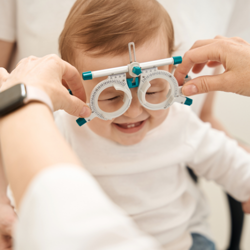 Małe dziecko podczas badania wzroku – zakładanie oprawy próbnej przez optometrystę.